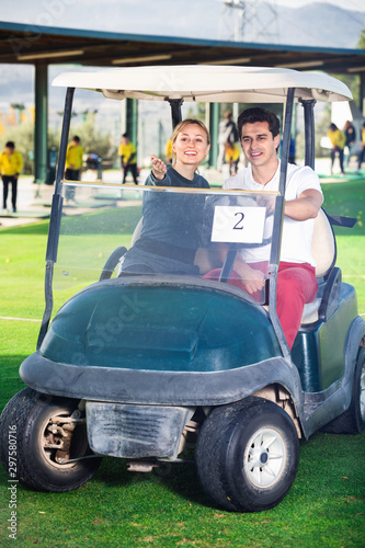 Male and female golf players driving golf cart at golf course