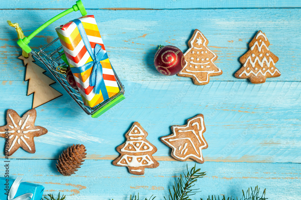 Colorful gift boxes shopping cart, fir, spruce toy cookies on a blue wooden background close up. The concept of preparing for the holidays New Year and Christmas.