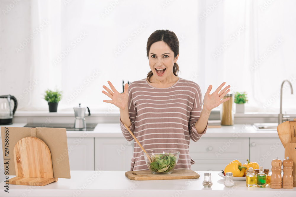 excited young woman showing wow gesture while standing near bowl with fresh vegetable salad excited young woman showing wow gesture while standing near bowl with fresh vegetable salad