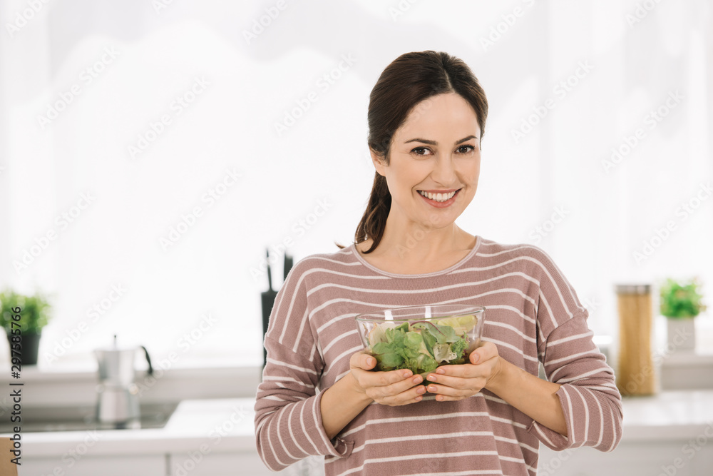 happy young woman smiling at camera while holding bowl with fresh vegetable salad happy young woman smiling at camera while holding bowl with fresh vegetable salad