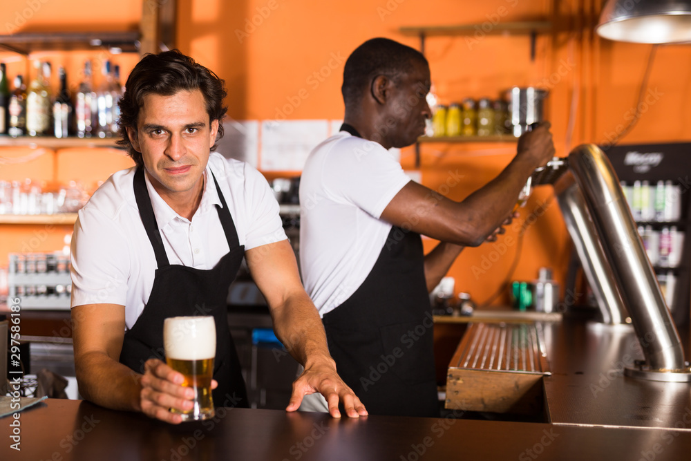 Bartender offering glass of beer, man pouring beer on background