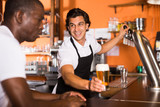 Positive man bartender giving glass of golden beer to man client