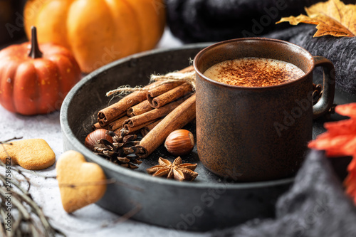 Thanksgiving concept - cup of hot frothy coffee in a rustic brown mug with cinnamon sticks, hazelnuts, wool shawl, orange pumpkins and autumnal leaves