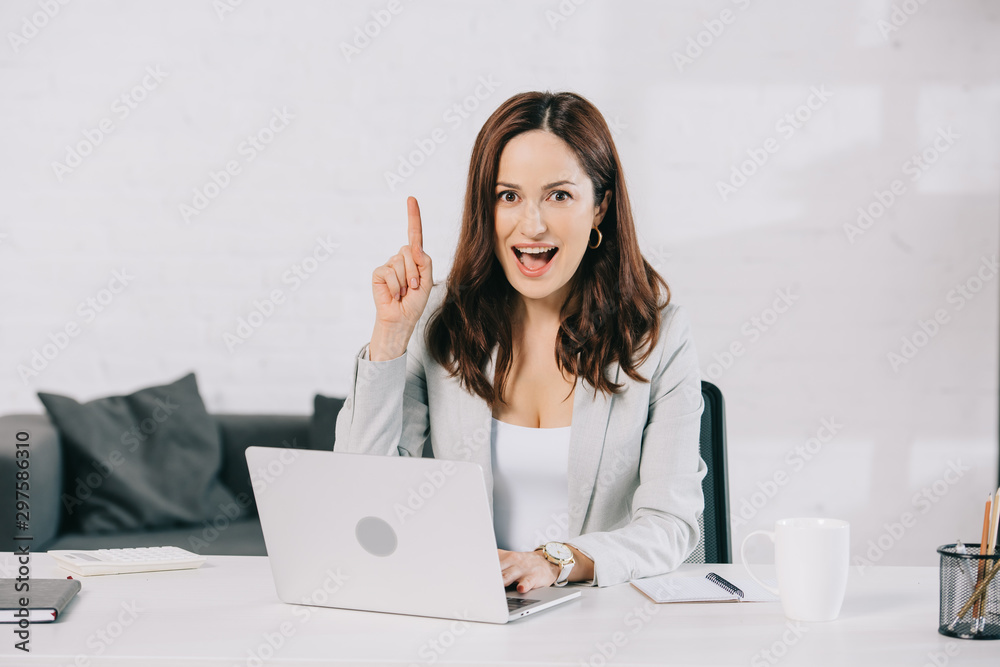 excited young secretary showing idea sign while sitting at workplace in office excited young secretary showing idea sign while sitting at workplace in office