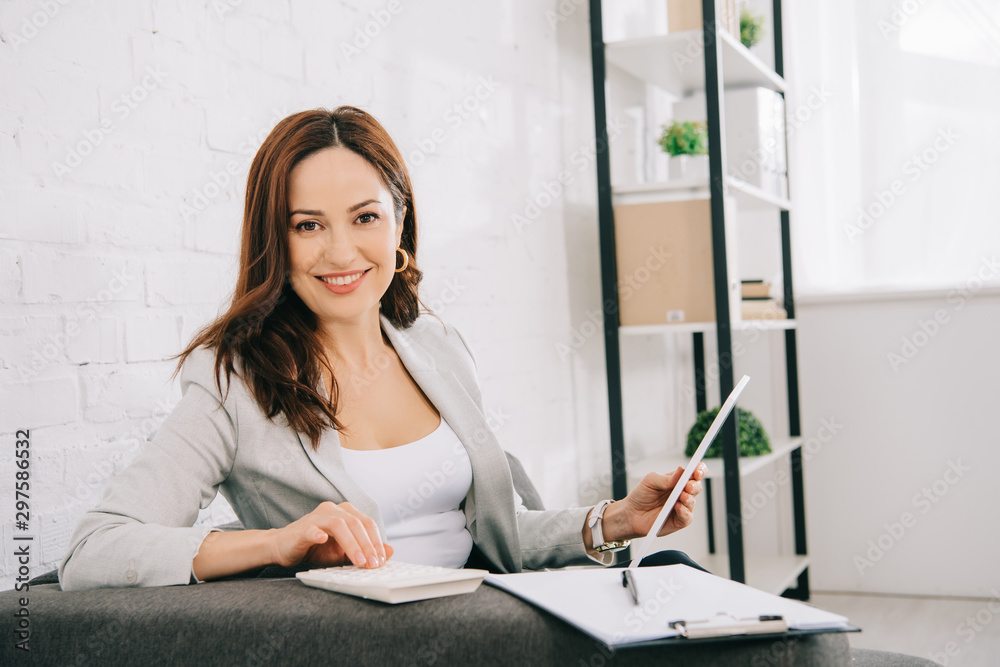 cheerful young secretary looking at camera while sitting on couch in office