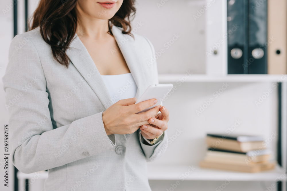partial view of elegant secretary using smartphone in office