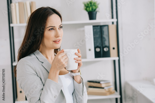 beautiful, pensive secretary looking away while holding coffee cup