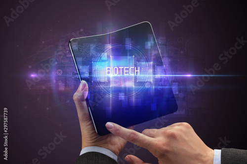 Businessman holding a foldable smartphone with BIOTECH inscription, new technology concept