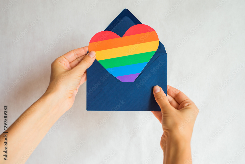 Woman holds in hands envelope and heart in the colors of the rainbow. Young beautiful girl. LGBT pride month. Coming out. Lesbian Gay Bisexual Transgender. LGBTQ+ flag. Love, human rights, tolerance