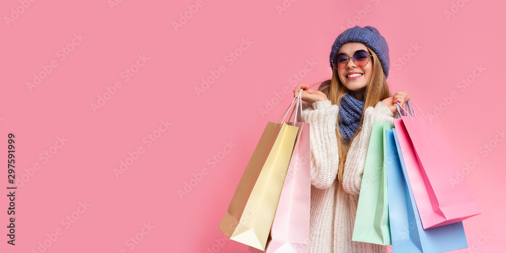 Positive girl in knitted hat and sunglasses holding shopping bags
