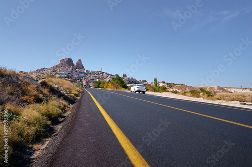 Highway to home. White automobile stopped at a sideway on a road in the desert leading to a town on a hill. Uçhisar, Cappadocia, Turkey. © luengo_ua