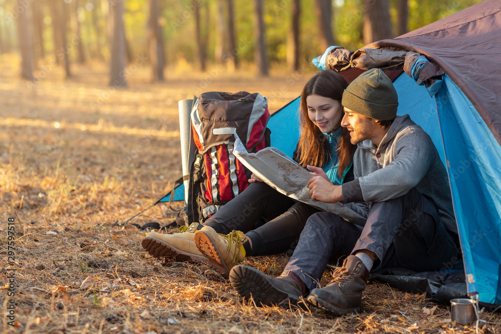 Romantic couple camping outdoors, sitting in tent and checking map Romantic couple camping outdoors, sitting in tent and checking map