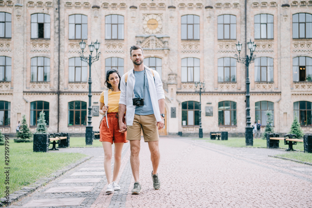 happy coupe holding hands while walking near building