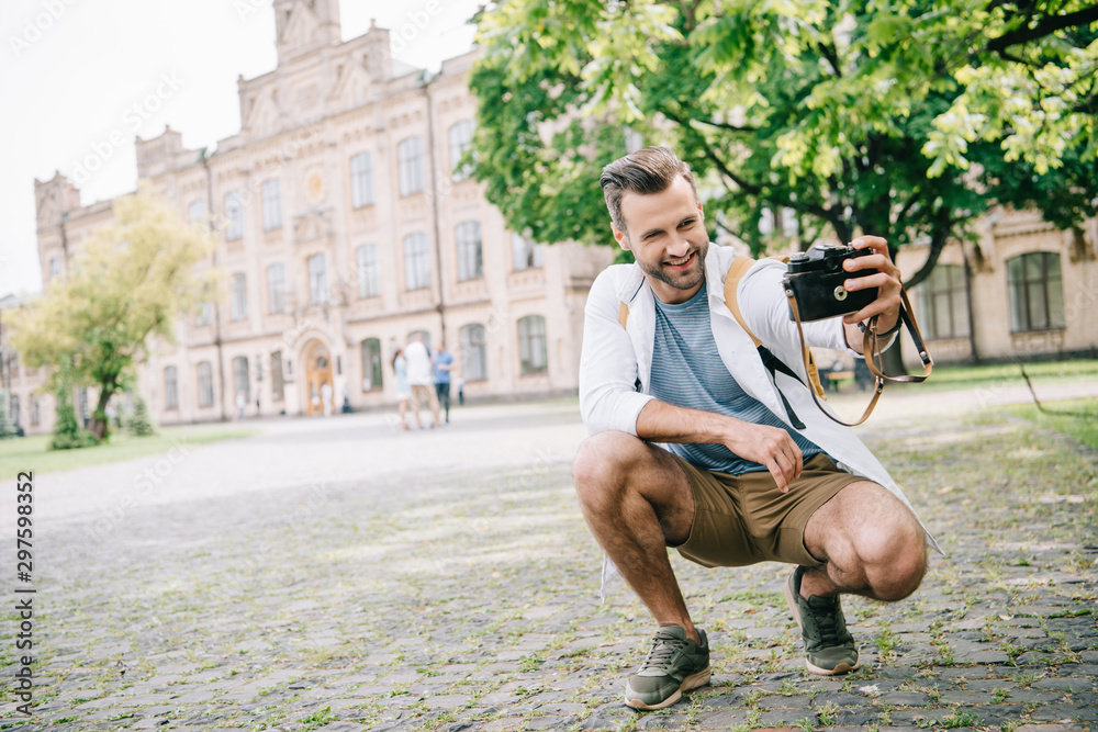 cheerful bearded man taking selfie on digital camera near building