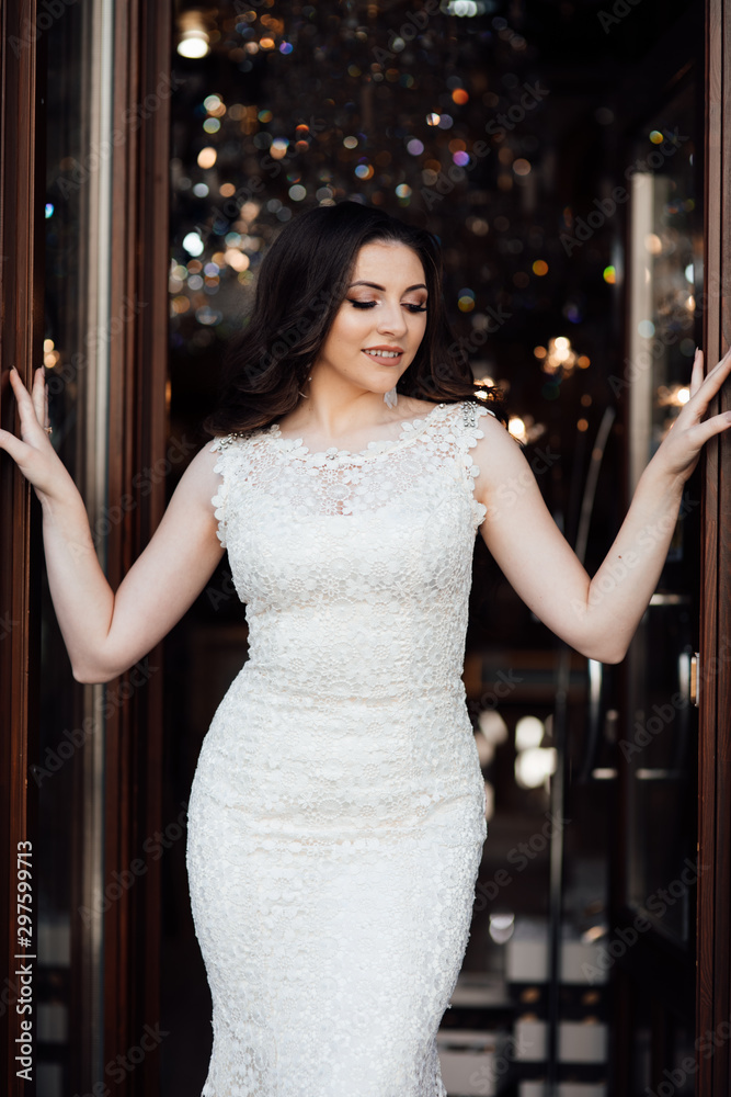 Portrait of cute brunette girl with long-haired posing on the way out on terrace in restaurant. She wears white dress and looks happy. Beauty portrait of female face with natural skin and health hair Portrait of cute brunette girl with long-haired posing on the way out on terrace in restaurant. She wears white dress and looks happy. Beauty portrait of female face with natural skin and health hair