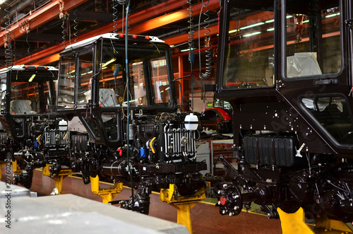 Tractor Manufacture work. Assembly line inside the agricultural machinery factory. Installation of parts on the tractor body - Image © MaxSafaniuk