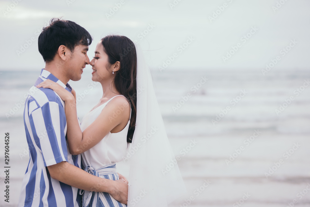 Obraz premium Valentine day - Young couple lover are having a warm and romantic moment at sunset on the beach background. Happy smiling couple kissing on the sea background.