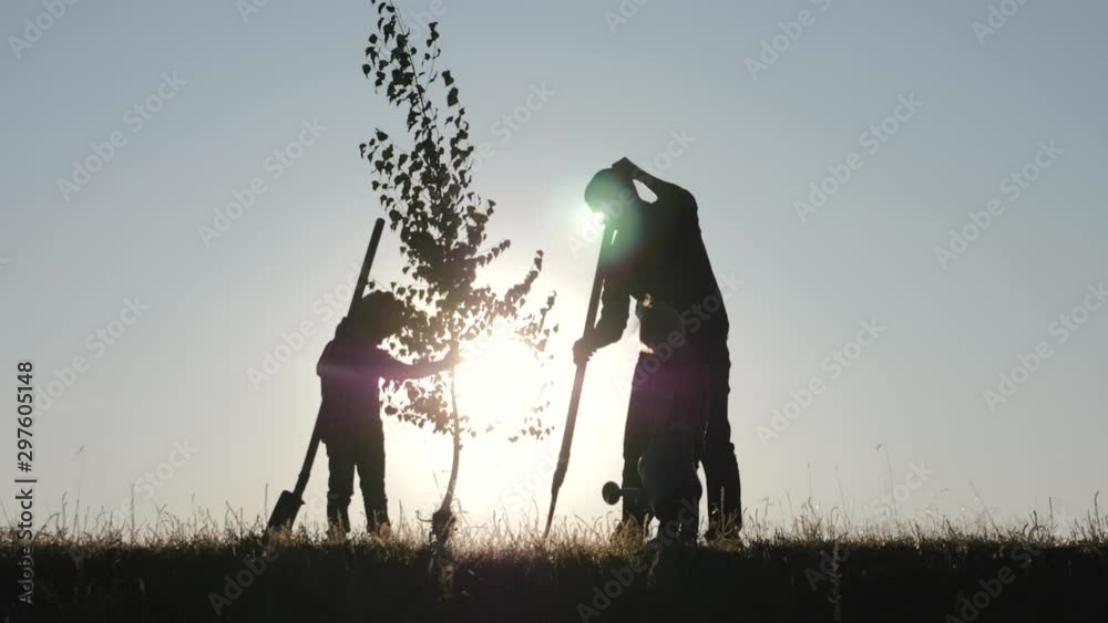 A happy family of farmers. Silhouette of a father and two children planting and watering a tree in the Park at sunset.