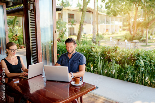 Coworking and freelance concept. Young  bearded man  and young woman working together on laptop computer while sitting on cafe terrace.