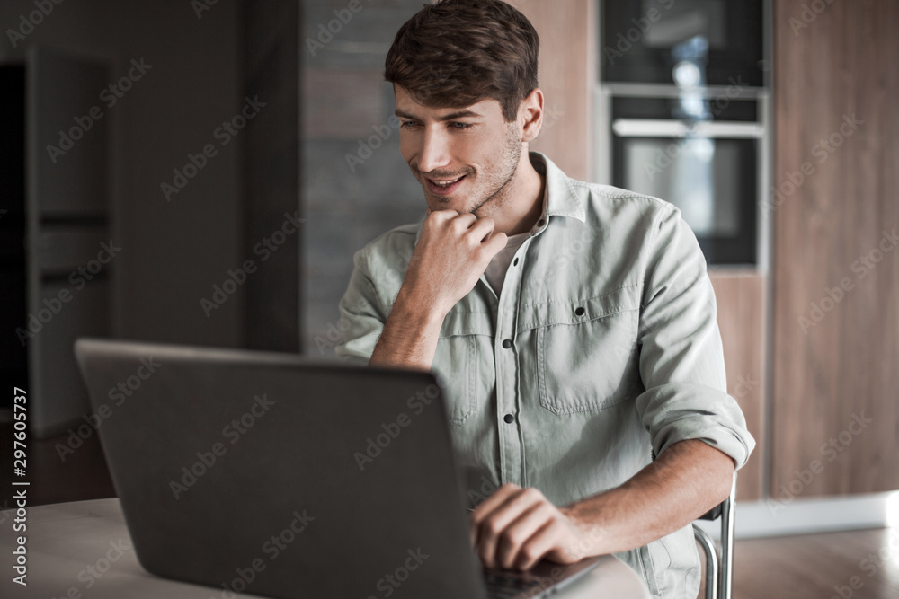 young man sitting in front of open laptop in kitchen young man sitting in front of open laptop in kitchen