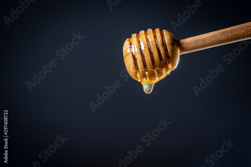 Wooden stick for honey with drop honey. Thick honey dripping and flowing down from the honey spoon on black background, close up