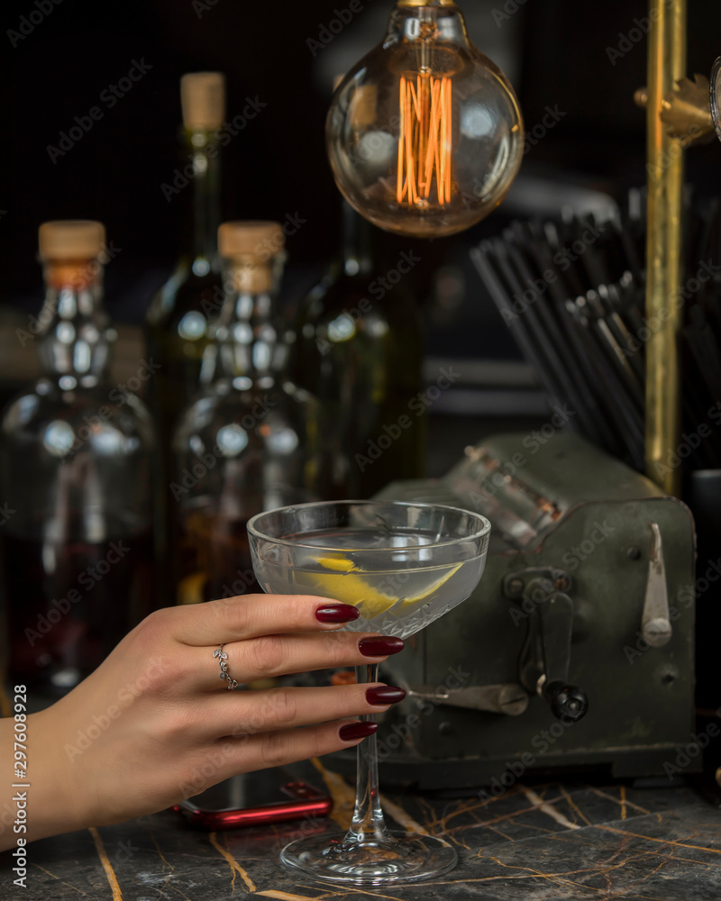 woman holds alcohol drink garnished with lemon skin in martini glass