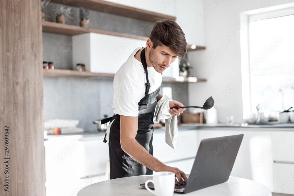 young man looking at laptop screen while cooking dinner