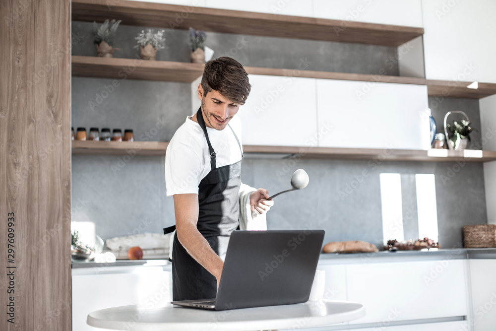 young man looking at laptop screen while cooking dinner young man looking at laptop screen while cooking dinner