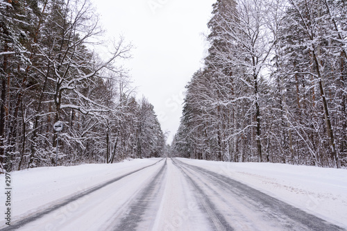 Patterns on the winter highway in the form of four straight lines. Snowy road on the background of snow-covered forest. Winter landscape.