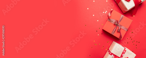 Creative composition with gifts or presents boxes with gold bows and star confetti on red background top view. Flat lay composition for birthday, christmas or wedding.