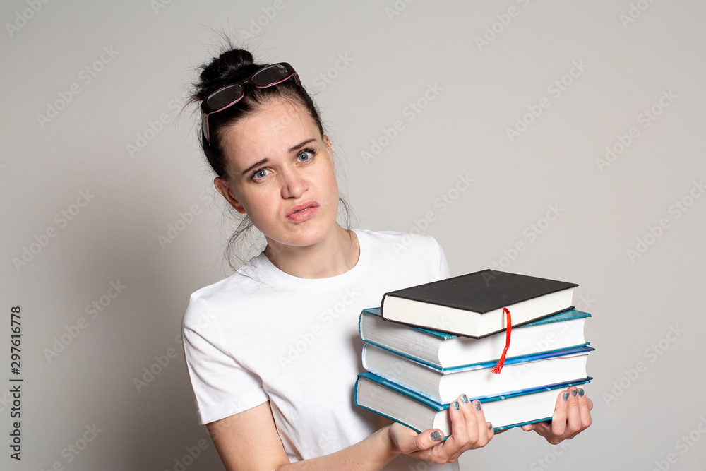 Cute, puzzled student with glasses on head holds a stack of books in hands and looks anxiously at the camera. Cute, puzzled student with glasses on head holds a stack of books in hands and looks anxiously at the camera.