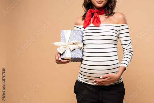 cropped view of pregnant woman holding gift on beige background