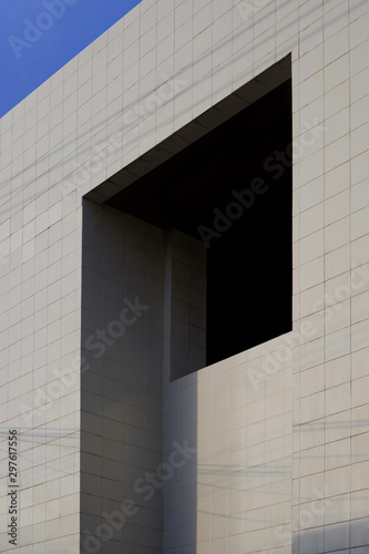 Rectangle pattern of gray tiles wall of modern building with sunlight and shadow of cable lines on building surface with blue sky, side view and vertical frame 