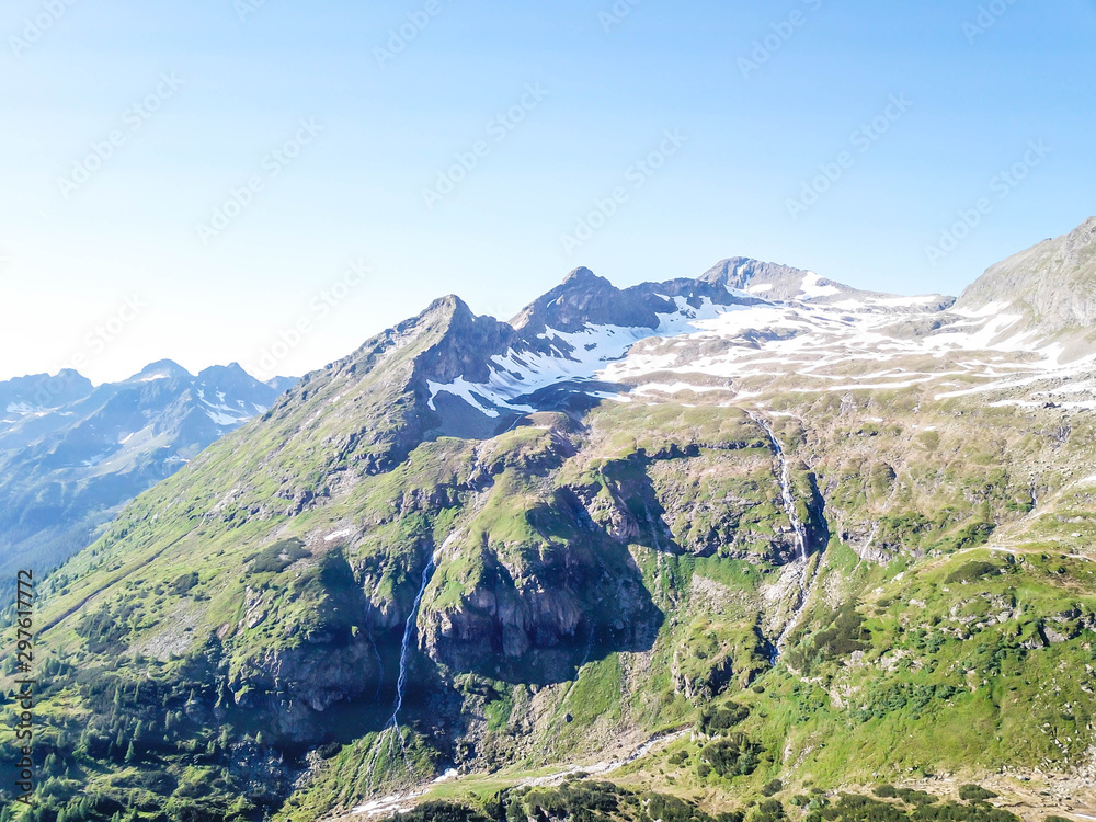 A panoramic view on Schladming Alps, partially still covered with snow. Spring slowly reaching the tallest parts of the mountains. Sharp peaks, slopes partially overgrown with lush green plants.