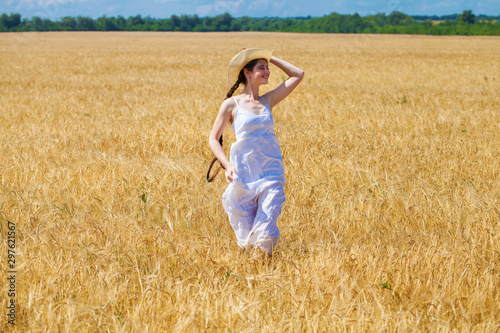 Young brunette woman in white dress walking in a wheat field