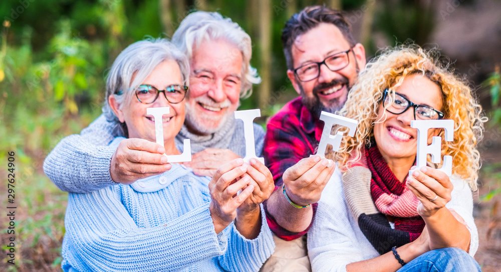 Group of four caucasian people family together with life blocks posing happy and cheerful -defocused backgroud of outdoor nature forest - save planet and enjoy lifestyle concept Group of four caucasian people family together with life blocks posing happy and cheerful -defocused backgroud of outdoor nature forest - save planet and enjoy lifestyle concept