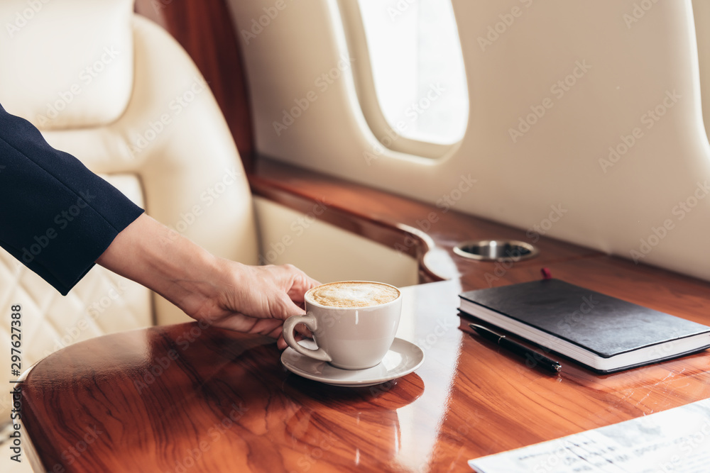 cropped view of flight attendant putting cup of coffee on table in private plane cropped view of flight attendant putting cup of coffee on table in private plane