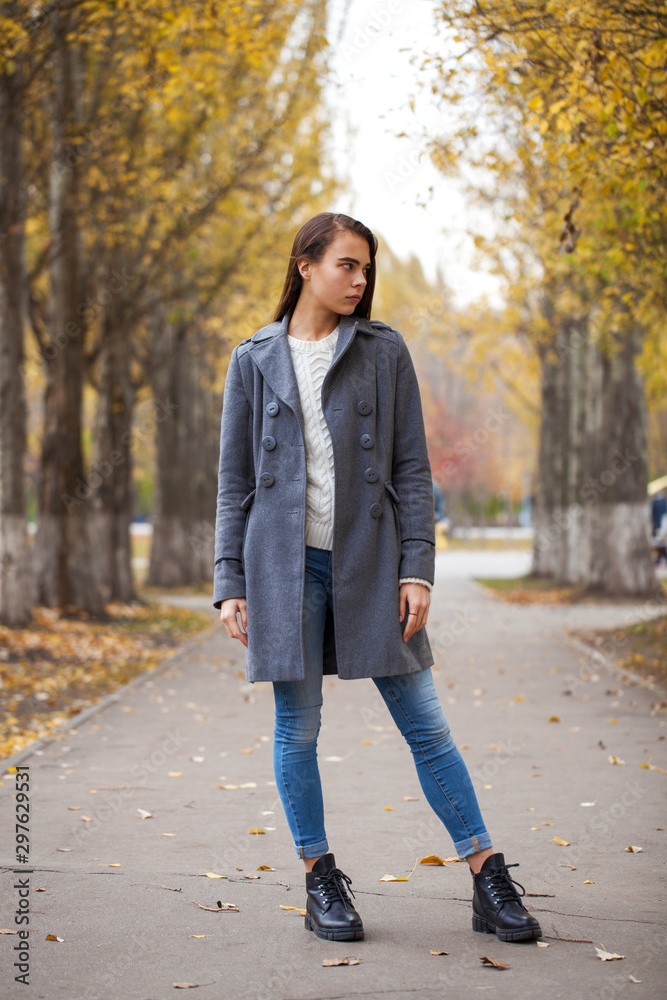Portrait of a young beautiful girl in blue jeans and gray coat