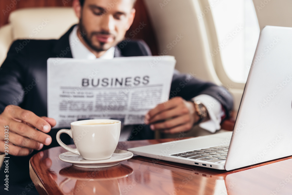 selective focus of businessman in suit reading business newspaper and taking cup in private plane selective focus of businessman in suit reading business newspaper and taking cup in private plane
