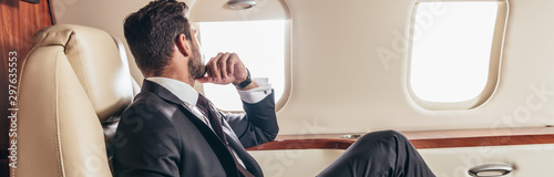 panoramic shot of businessman in suit looking through window in private plane photo