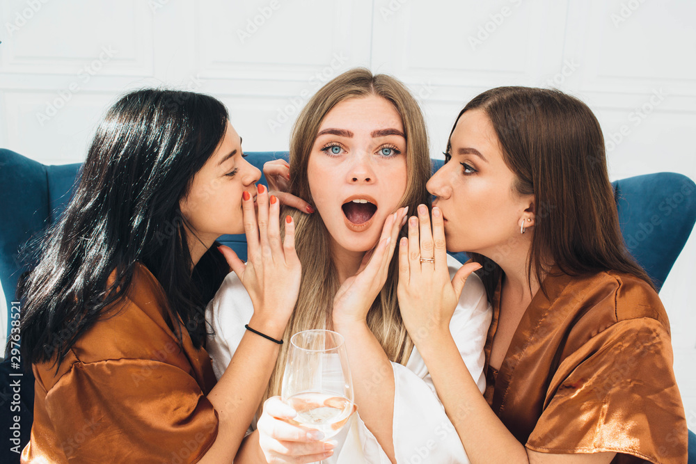 bridesmaids dressed in satin robes tell her shocking news in her ear. Bachelorette weekend bridesmaids dressed in satin robes tell her shocking news in her ear. Bachelorette weekend