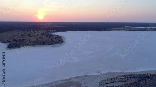 Flying over shallow salt lake towards the orange sun at sunset. photo