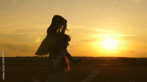little daughter riding on mom's shoulders in sunset, walk in park in summer. young family with baby, in field.