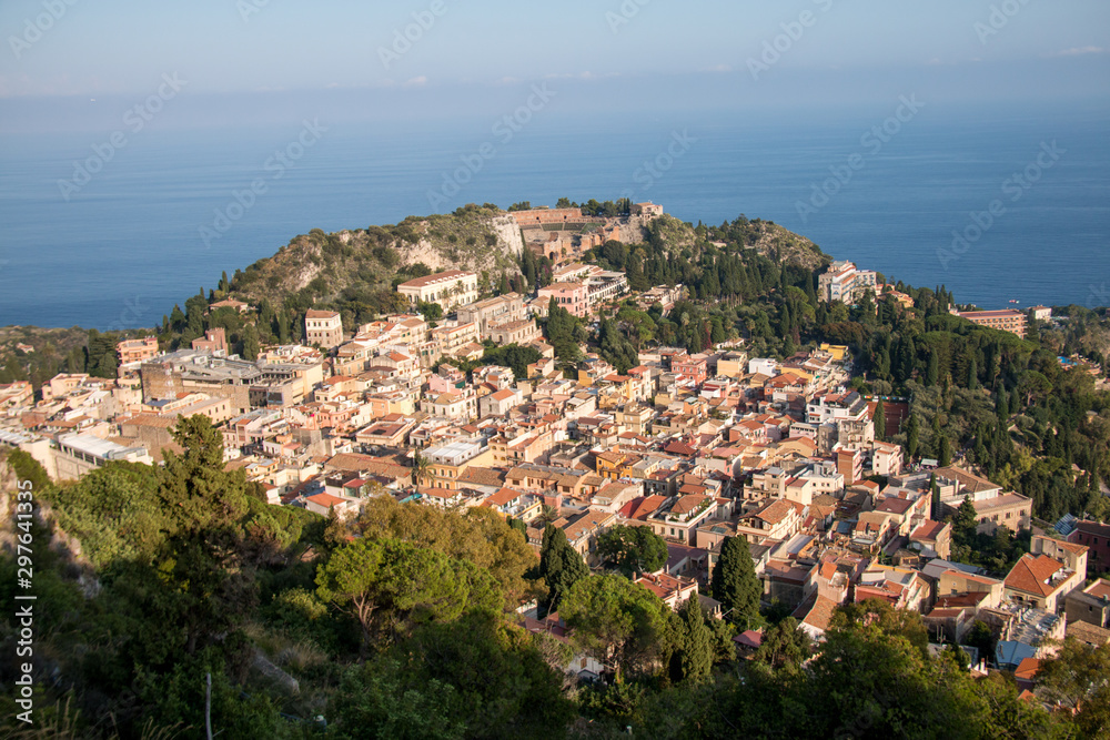 Beautiful panorama from mountain top to a small mediterranean sicilian town, Taormina, in warm sunset with the sea in the background, Sicily, Italy