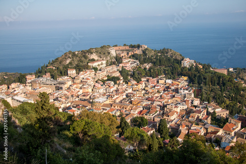 Beautiful panorama from mountain top to a small mediterranean sicilian town, Taormina, in warm sunset with the sea in the background, Sicily, Italy © JKn