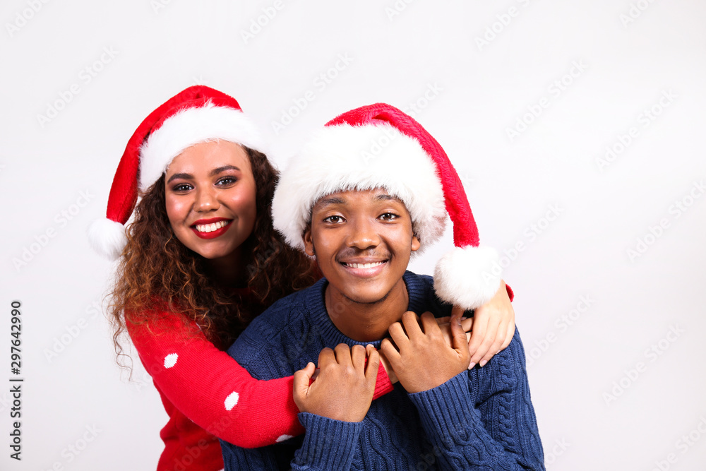 Studio portrait of young couple, boyfriend & girlfriend with dark skin wearing santa claus hat and christmas outfit. Ugly sweater concept. Close up, copy space for text, isolated background. Studio portrait of young couple, boyfriend & girlfriend with dark skin wearing santa claus hat and christmas outfit. Ugly sweater concept. Close up, copy space for text, isolated background.