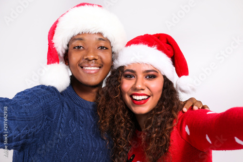 Studio portrait of young couple  boyfriend   girlfriend with dark skin wearing santa claus hat and christmas outfit. Ugly sweater concept. Close up  copy space for text  isolated background.