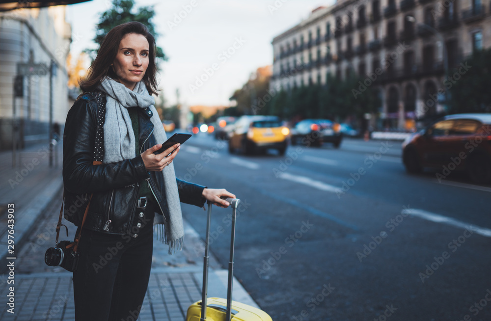 Traveler woman with suitcase calling mobile phone waiting yellow auto taxi in evening street europe city Barcelona. Girl tourist using smartphone technology internet online gadget cellphone - obrazy, fototapety, plakaty 