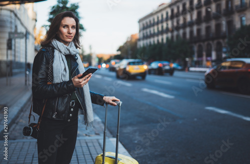 Traveler woman with suitcase calling mobile phone waiting yellow auto taxi in evening street europe city Barcelona. Girl tourist using smartphone technology internet online gadget cellphone