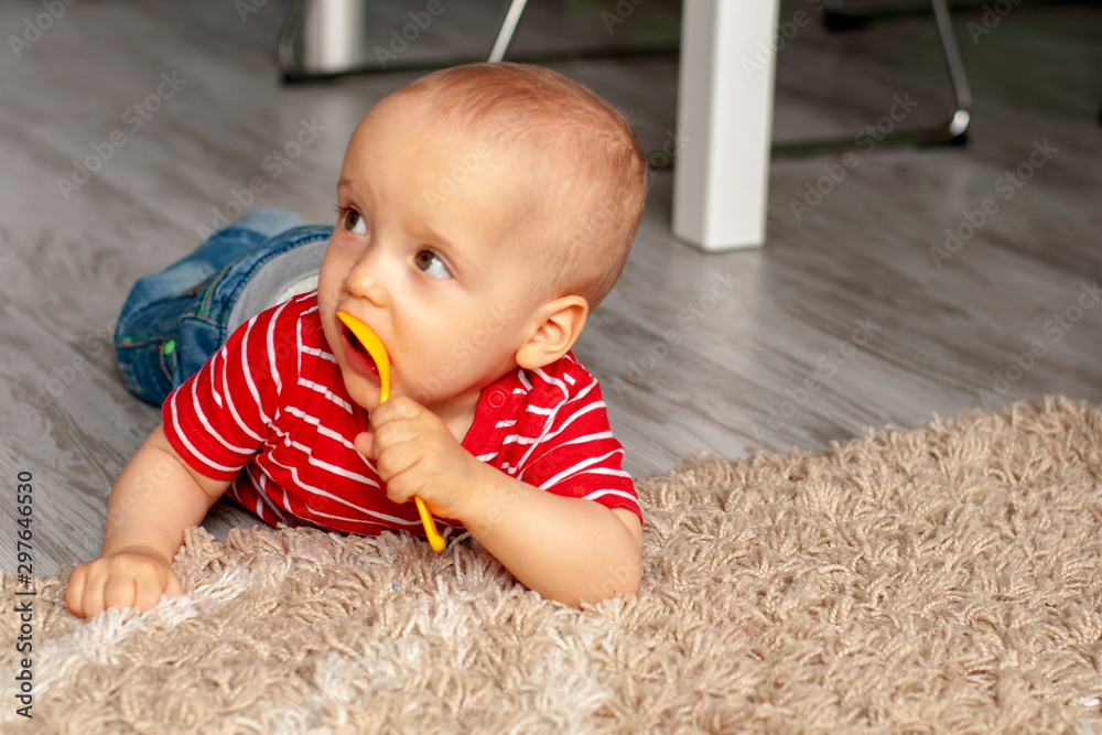 Training, use of cutlery. Baby thought and chews a spoon lying on the carpet. Teaching babies Training, use of cutlery. Baby thought and chews a spoon lying on the carpet. Teaching babies